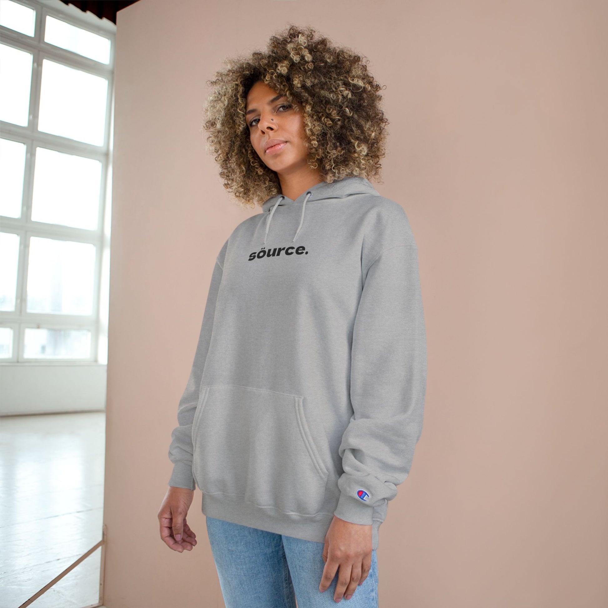Person wearing a gray hoodie with 'source.' text against a beige wall.